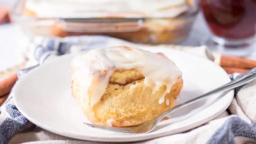 A fluffy cinnamon roll on a plate, with frosting.