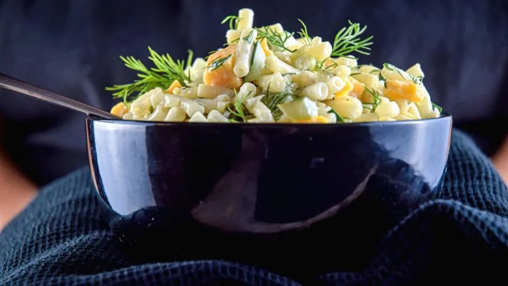 A bowl of pasta salad with pickles and cheese.