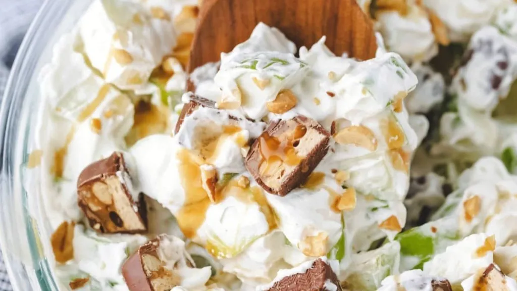 A bowl of snickers apple salad with a wooden spoon inside.