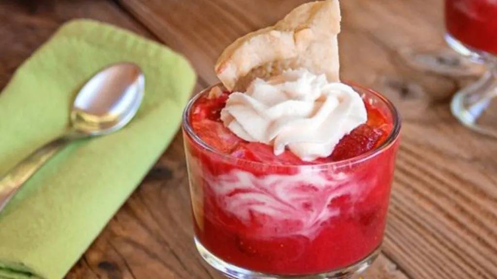 A glass filled with strawberry pie filling, topped with whipped cream and pie crust.