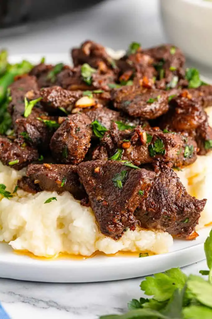 Garlic butter steak bites served over mashed potatoes on a white serving plate.