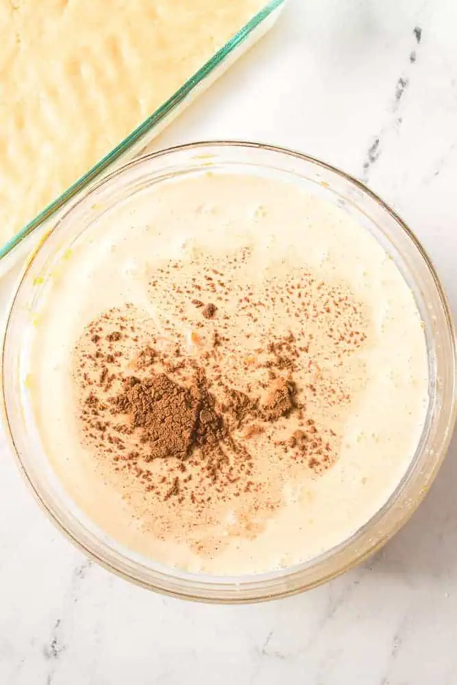 Glass mixing bowl with pumpkin pie dessert bar filling and evaporated milk and pumpkin pie spice added.