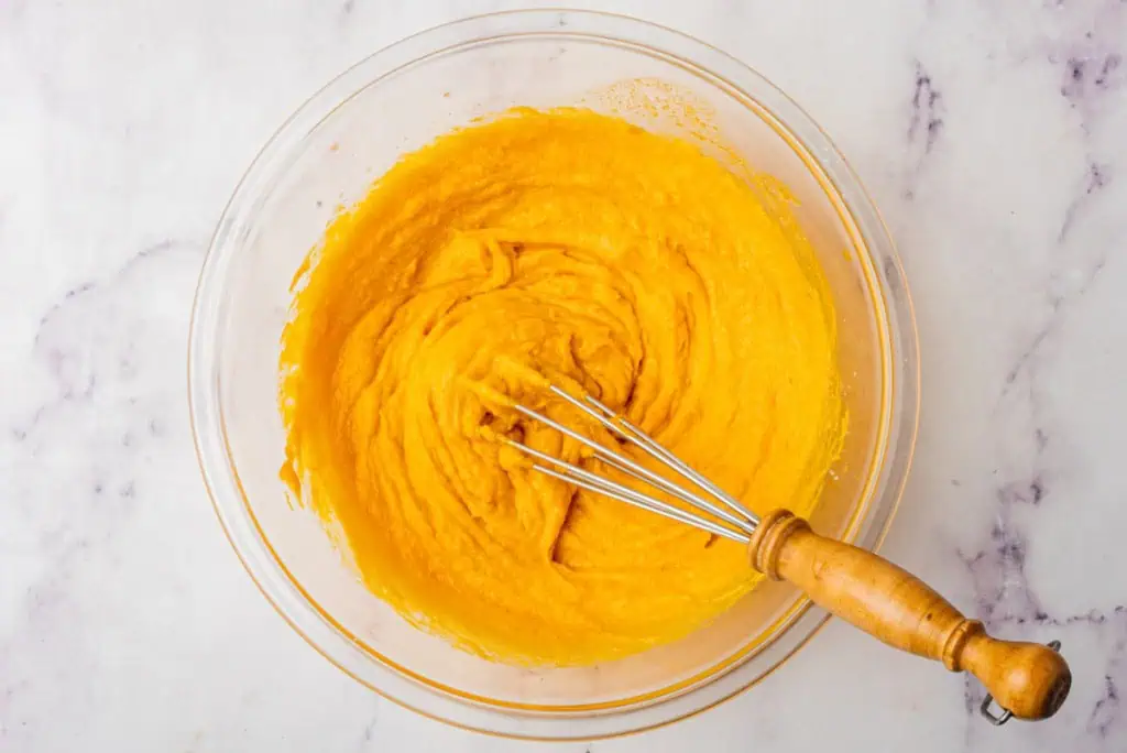 Glass mixing bowl with pumpkin puree cookie mixture and a small metal whisk.