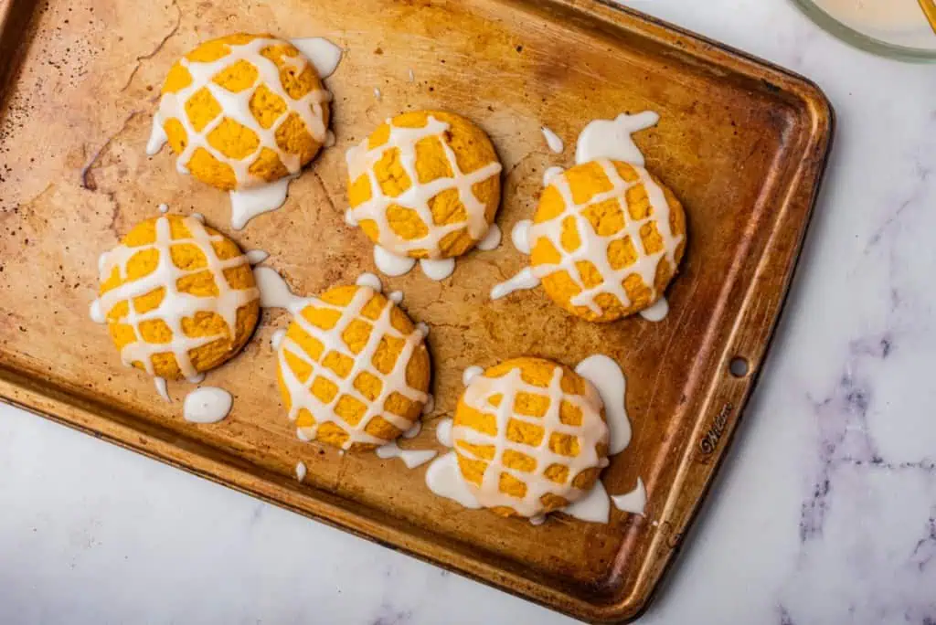 Metal baking tray with baked pumpkin cookies, drizzled with a sugar glaze.
