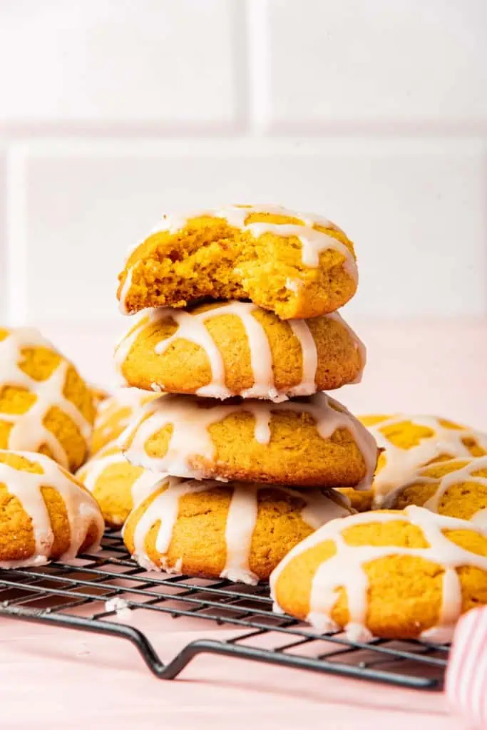 Close up of stacked soft pumpkin cookies on a metal rack, bite taken from the top cookie.
