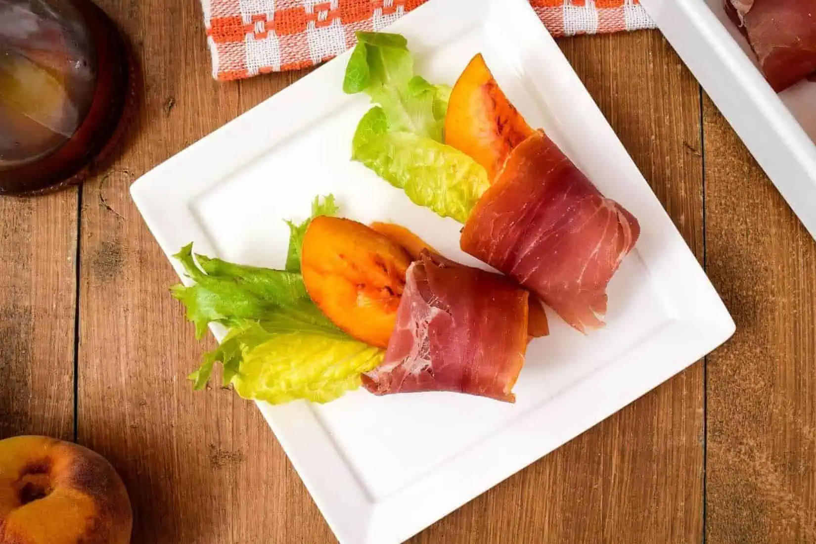 a peach tucked into lettuce leaves and wrapped with prosciutto.
