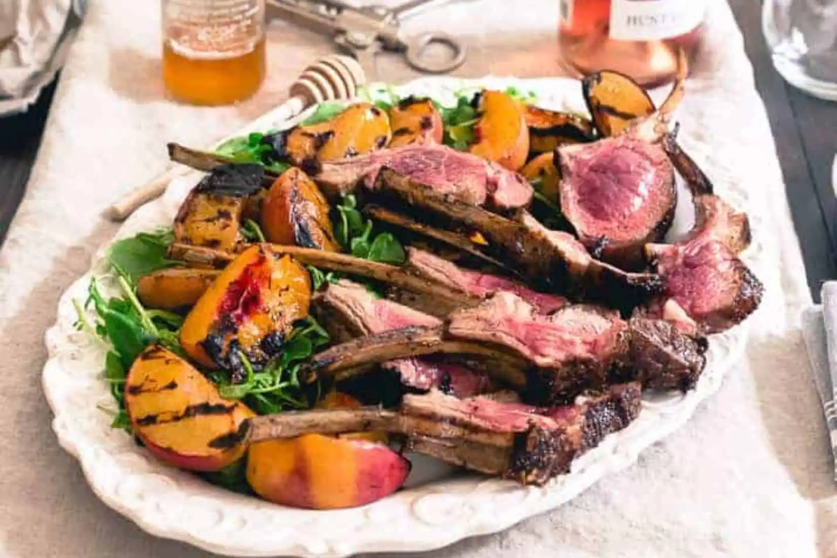 A platter of grilled lamb chops with grilled peaches to the side.