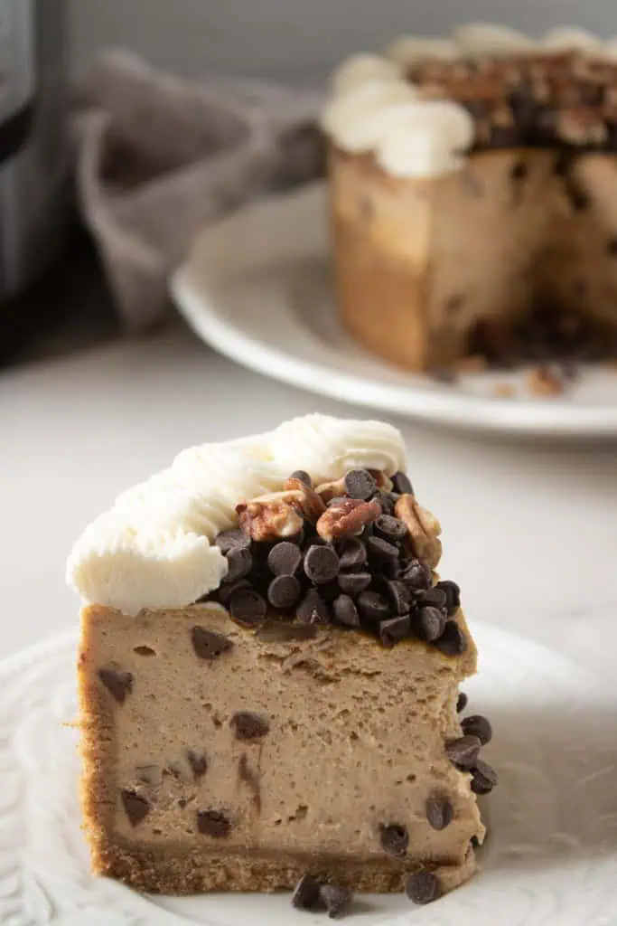 Close up of a slice of Instant Pot Pumpkin Chocolate Chip Cheesecake. Remainder of the cheesecake plated in the background.