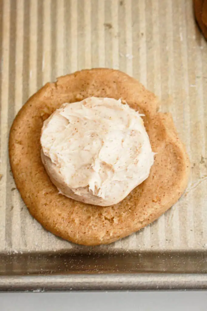 A flattened pumpkin cheesecake cookie dough disk with a frozen cream cheese dollop in the center.