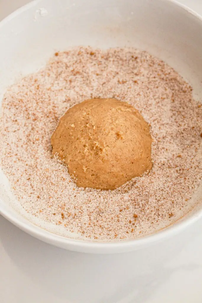 Small bowl with sugar and pumpkin spice. Assembled pumpkin cheesecake cookie rolled in the sugar spice mixture.