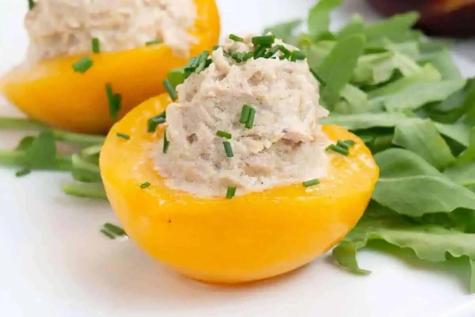 a peach half stuffed with tuna salad, on a plate.