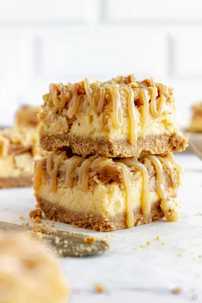 Close up of two stacked apple cheesecake bars resting on a sheet of parchment paper.