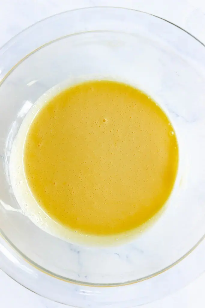 Glass bowl with whisked egg and dissolved sugar mixture.