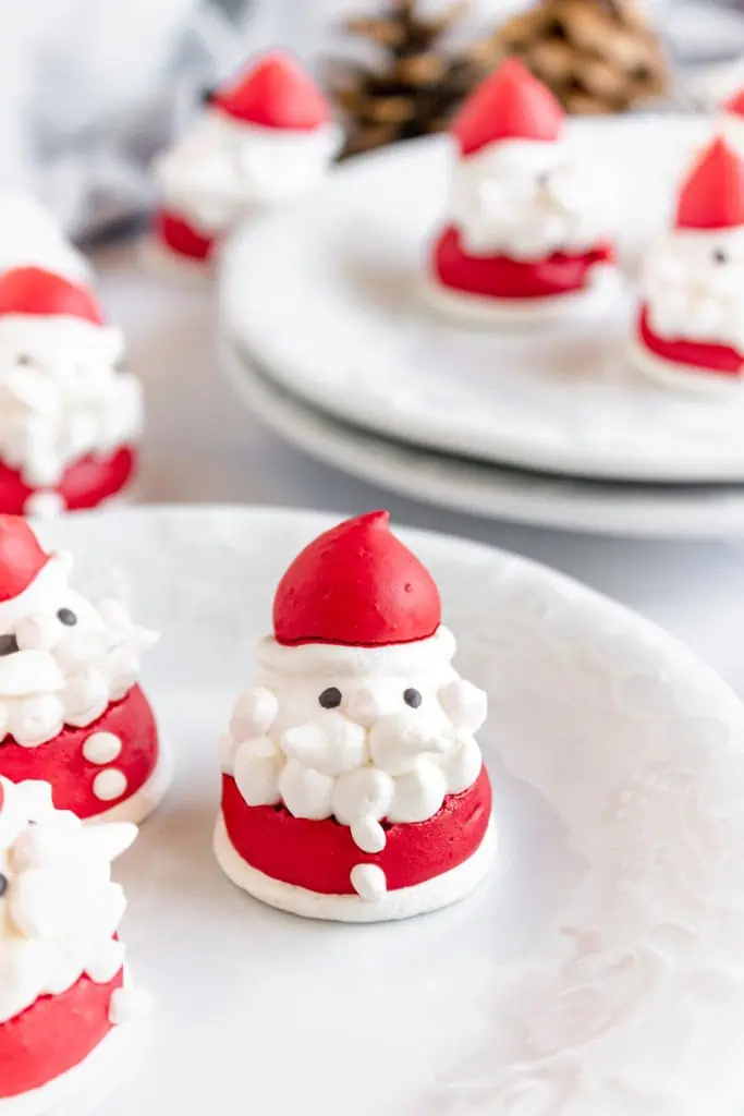 Santa Claus meringues on white serving plates with holiday table decoration in the background.