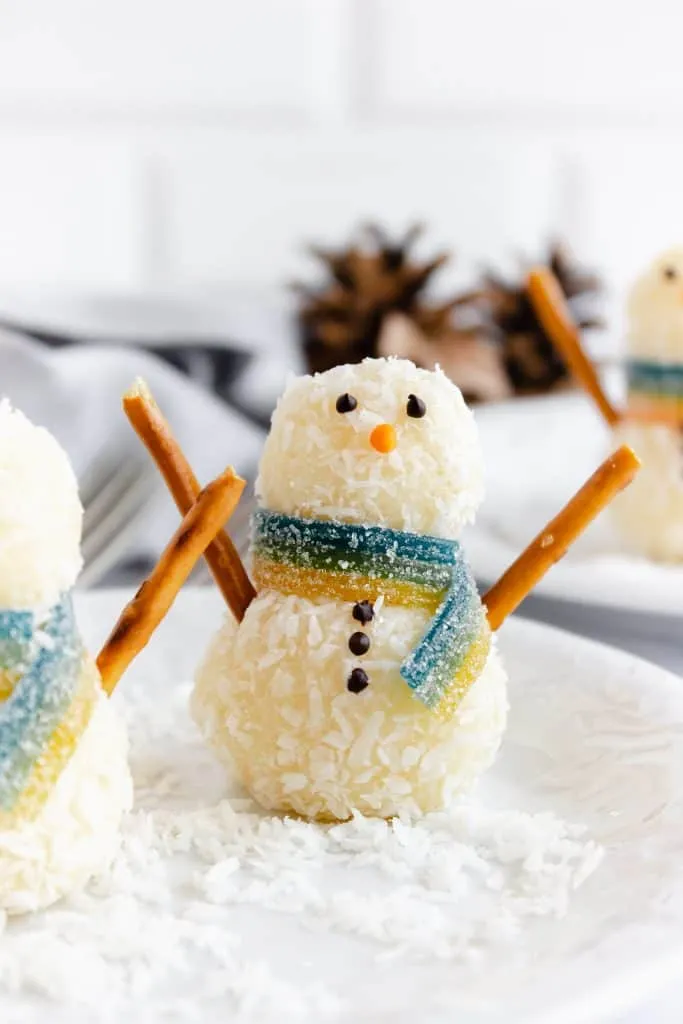 Close up of snowman truffles on a white serving plate with holiday decorations in the background.