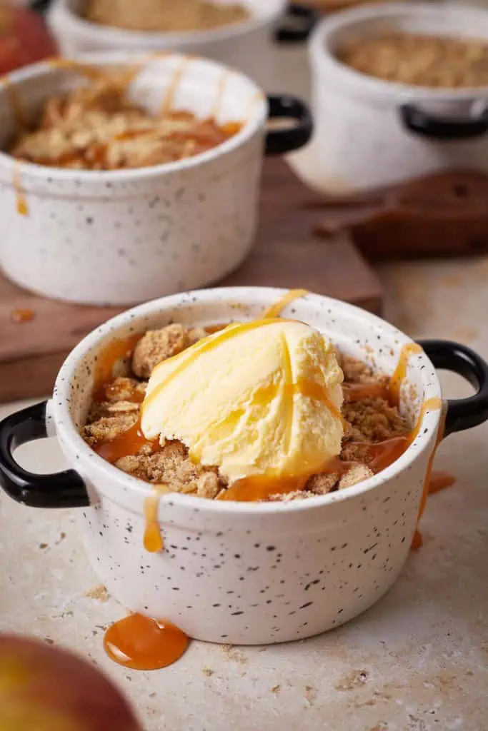 Close up of mini apple crisp in a ramekin, topped with a drizzle of caramel sauce and a scoop of ice cream.