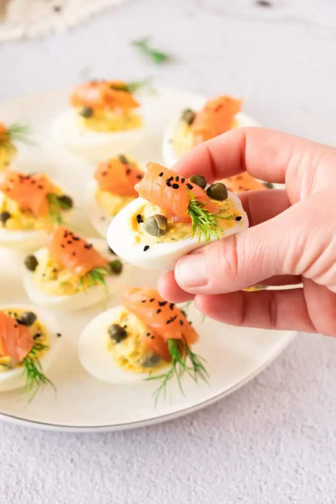 Platter of smoked salmon deviled eggs topped with dill and capers on a marble board.