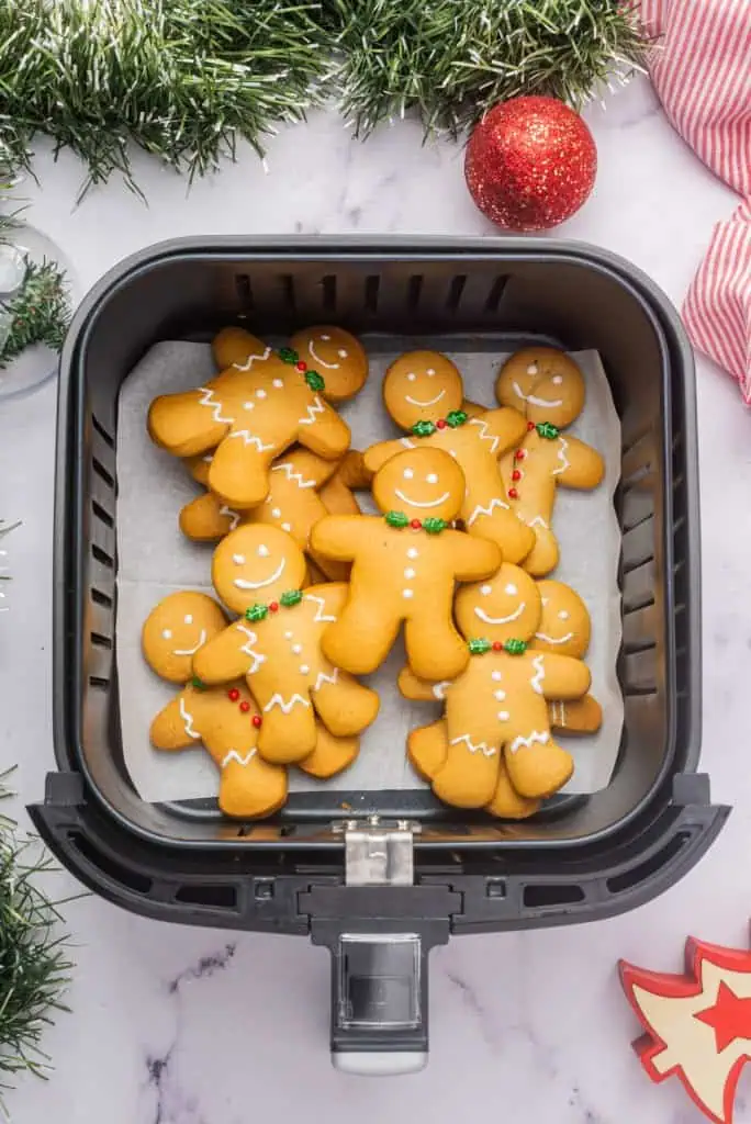 Air fryer gingerbread cookies in an air fryer basket on a marble countertop, Christmas decorations in the background.