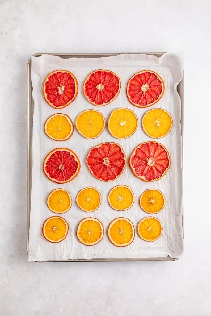 Dehydrated slices of orange and grapefruit on a baking sheet lined with parchment paper.