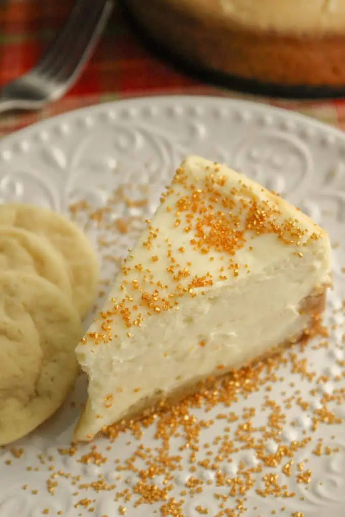 Close up of a slice of Instant Pot Sugar Cookie Cheesecake with three sugar cookies on a white serving plate.