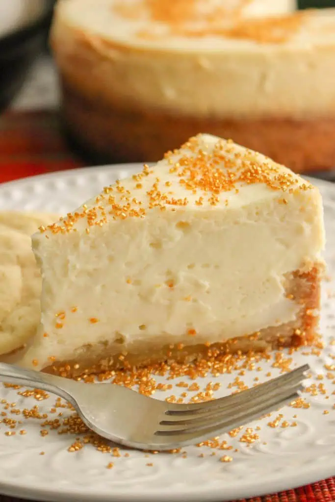 Close up of a slice of Instant Pot Sugar Cookie Cheesecake with three sugar cookies on a white serving plate, remainder of cheesecake in the background.