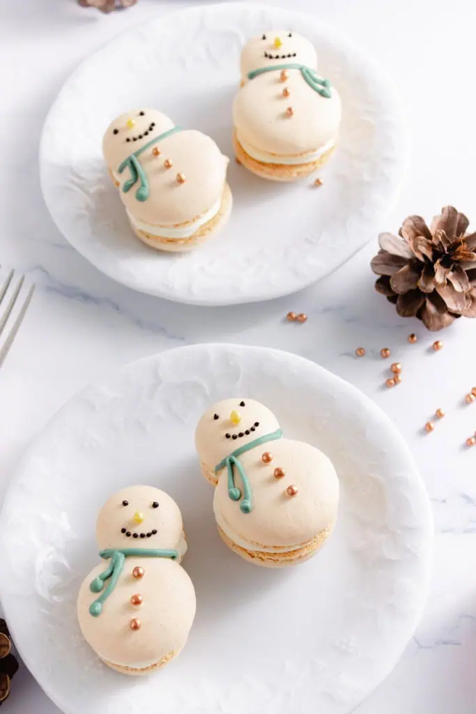 Overhead view of snowman macarons on white plates.