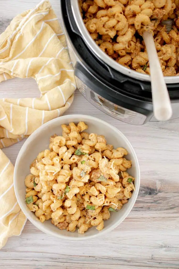 Overhead view of a bowl of Instant Pot cheesy garlicky pasta with remainder of pasta in the Instant Pot cooker with wooden serving spoon.