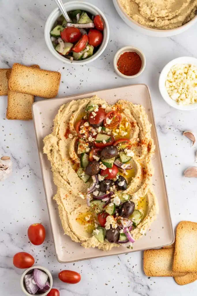 Mediterranean hummus on a platter plate with recipe ingredients scattered around on a marble countertop.