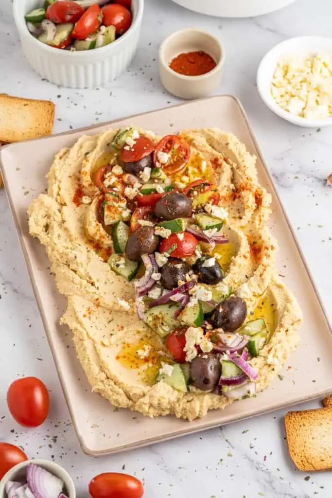Mediterranean hummus on a platter plate with recipe ingredients scattered around on a marble countertop.