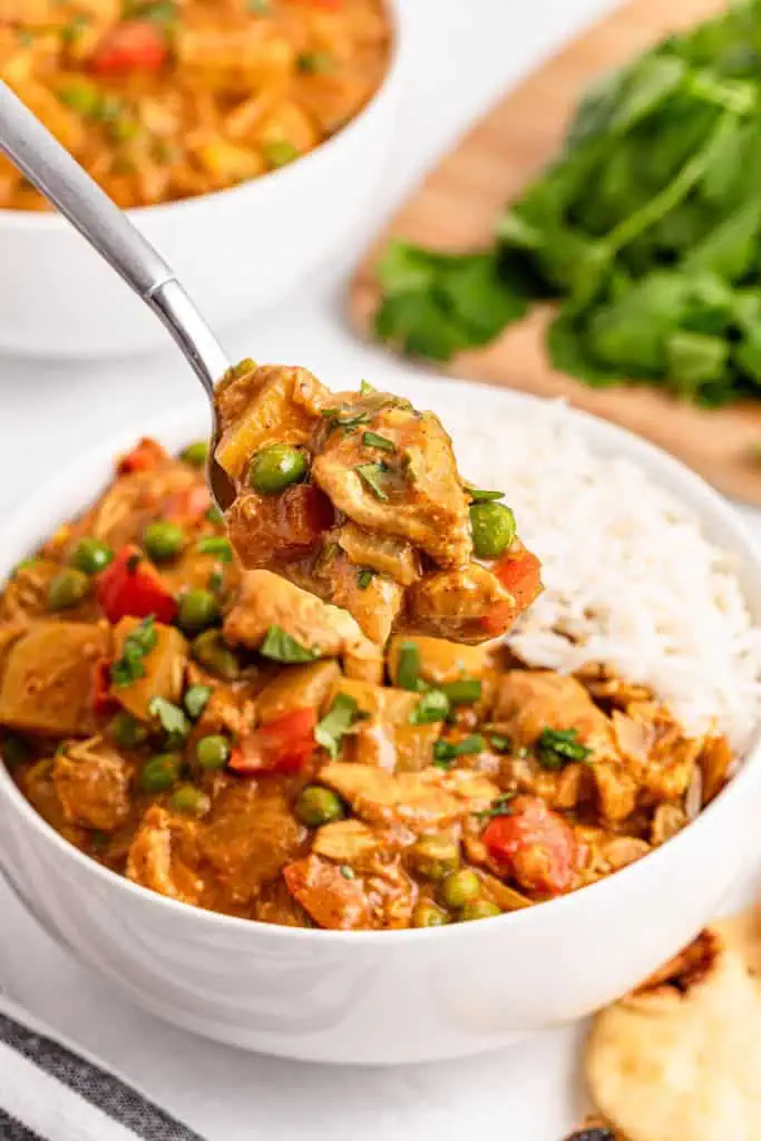 Close up of a bowl of Slow Cooker Chicken Curry with a spoon raised above holding the curry, another bowl of chicken curry in the background.