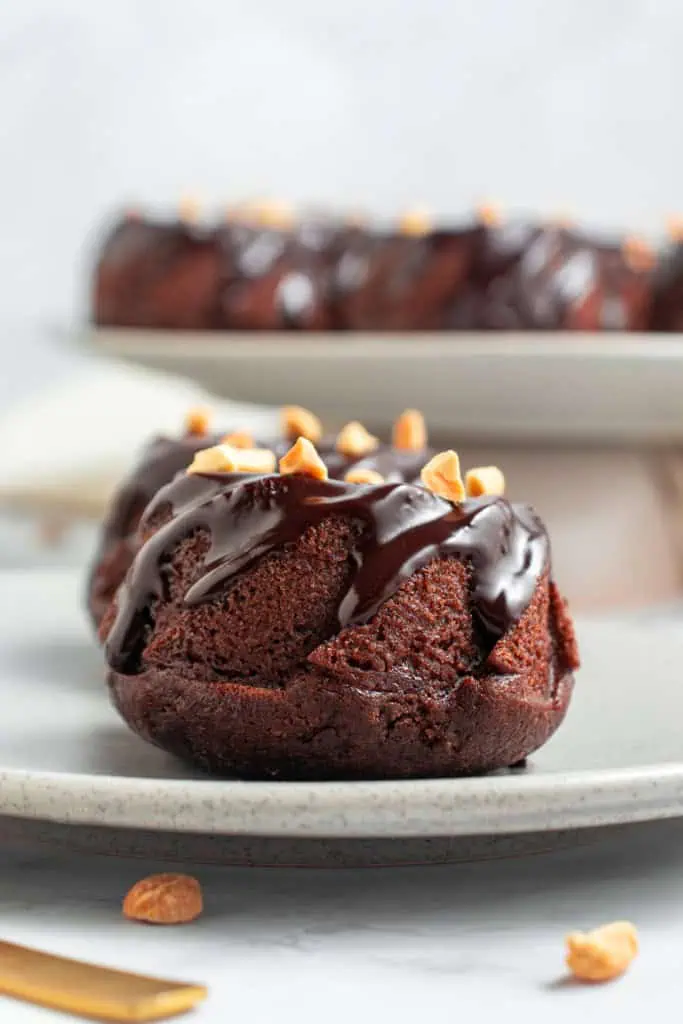 Close up of two mini chocolate bundt cakes on a serving plate with additional bundt cakes on a cake stand in the background.