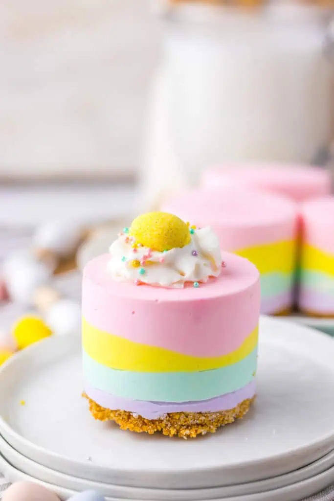 Close-up of a no bake Easter mini cheesecake on a stack of white plates with more mini cheesecakes in the background.