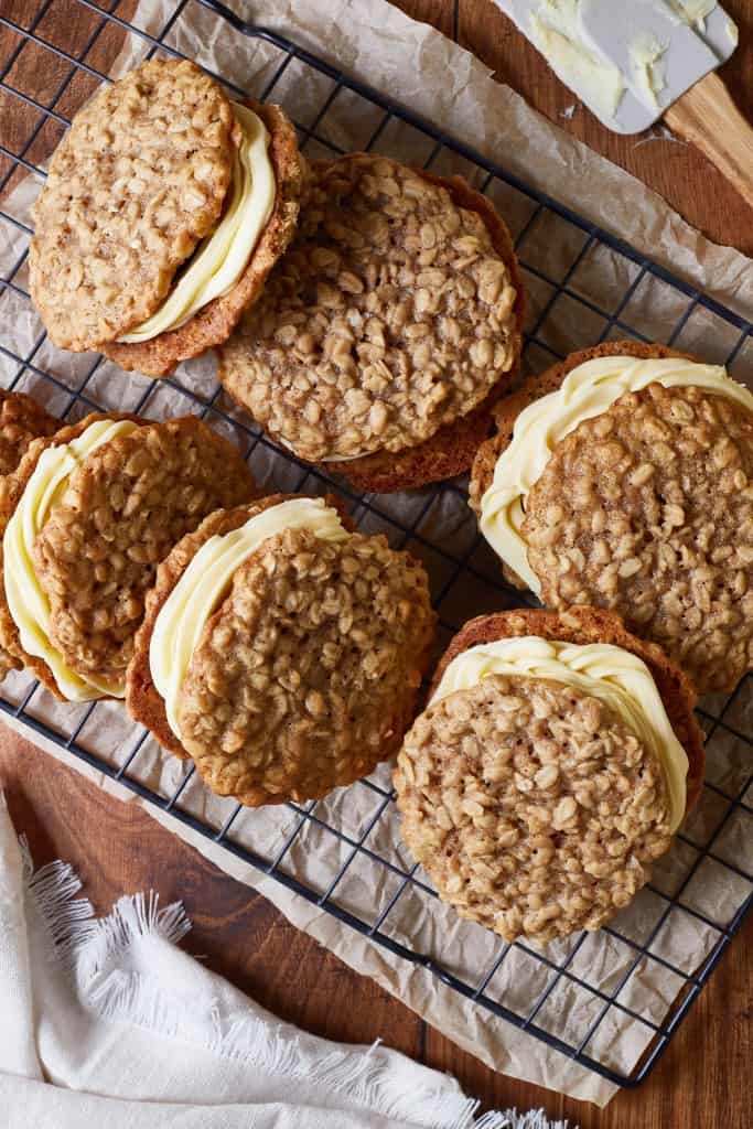 Assembled oatmeal cream pies on a wire rack with a rubber spatula to the side and parchment paper underneath.