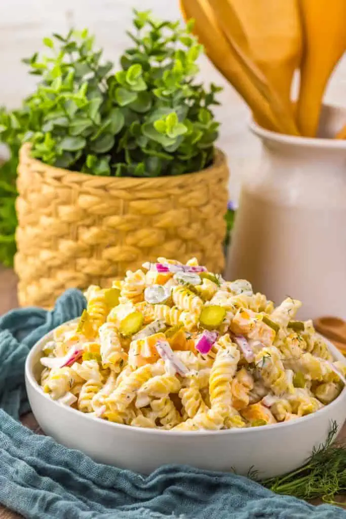 Pickle pasta salad ingredients in a glass bowl with the cream dressing next to it in a separate bowl on a marble countertop.