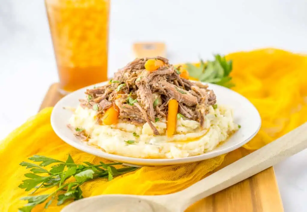 side view of creamy garlic mashed potatoes topped from tender pieces of shredded garlic herb pot roast