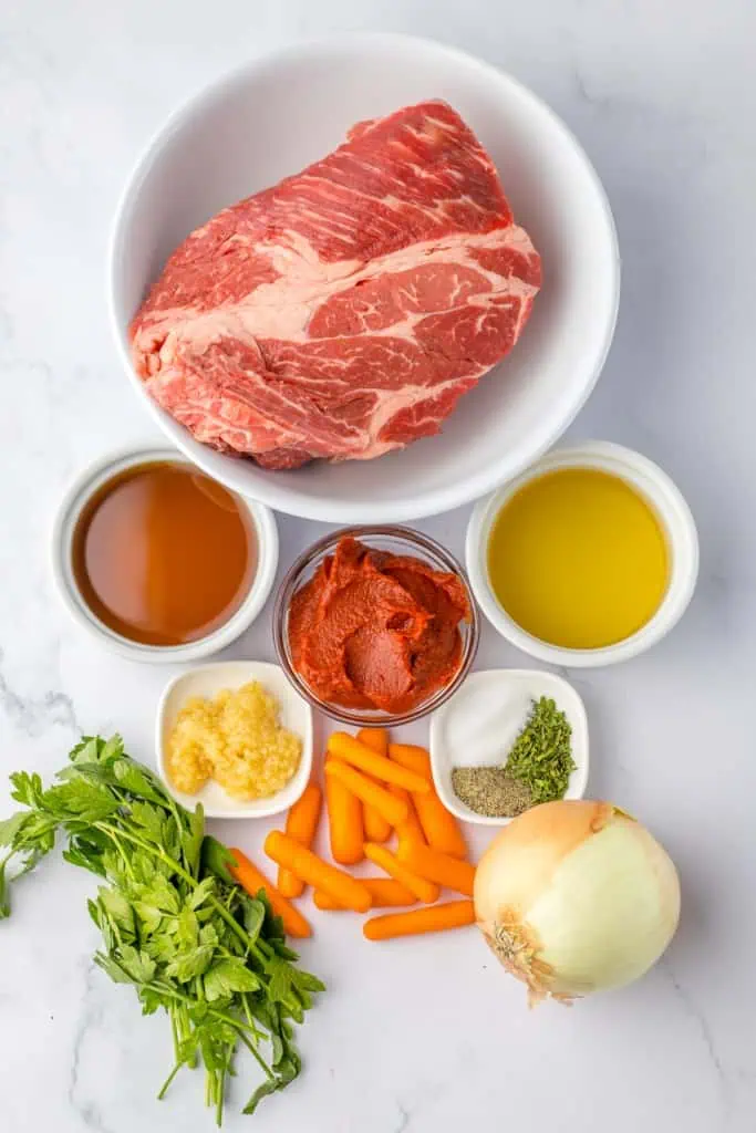 Ingredients to make slow cooker garlic herb pot roast on a marble countertop.
