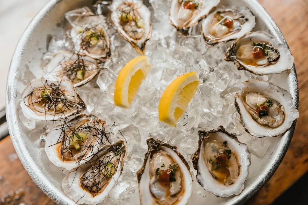 A bowl of fresh oysters on ice garnished with lemon wedges, showcasing seafood freshness.