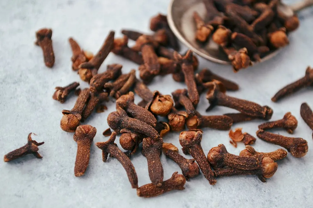 A close-up image of aromatic dry cloves scattered on a spoon over a gray surface.