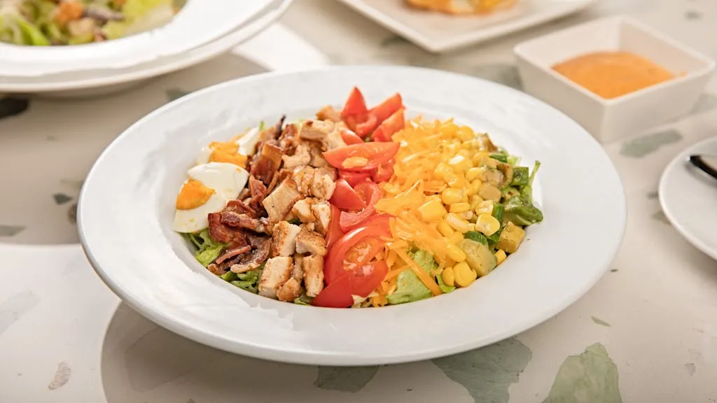 A vibrant Cobb salad with chicken, eggs, bacon, cheese, and vegetables on a table.