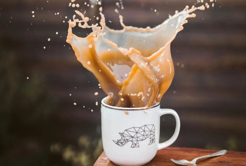 Capture of a vibrant coffee splash in a white mug with geometric bear design, evoking energy and movement.