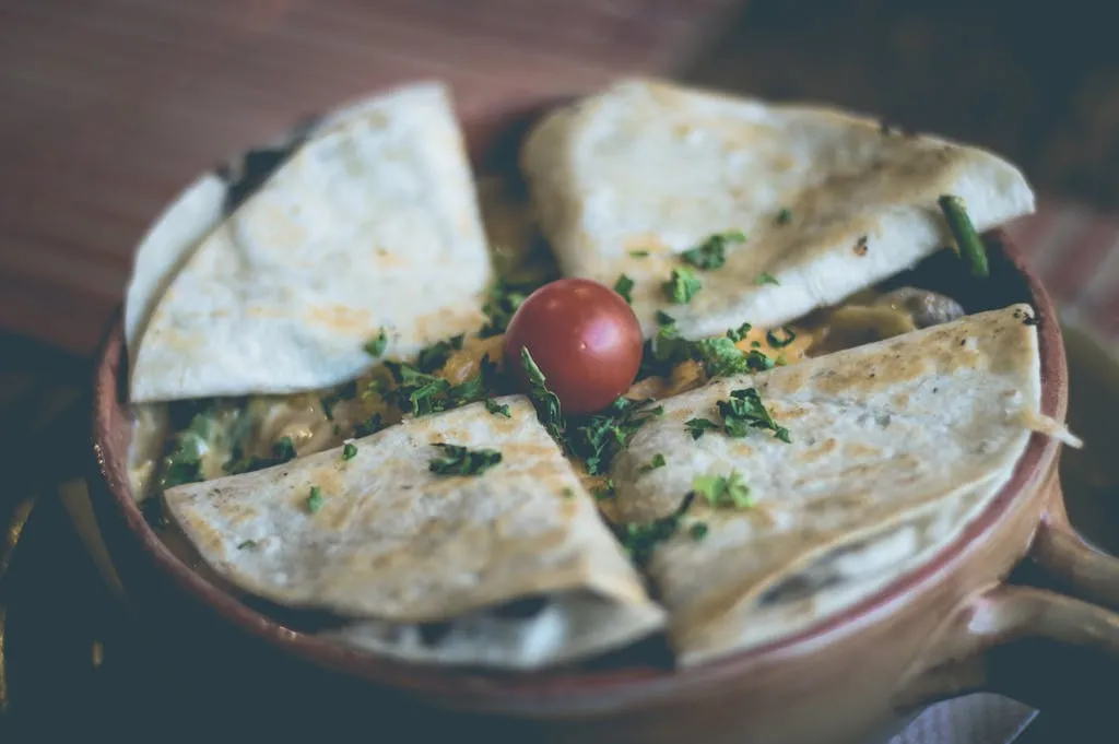 Close-up of a tasty quesadilla garnished with fresh parsley and a ripe cherry tomato.