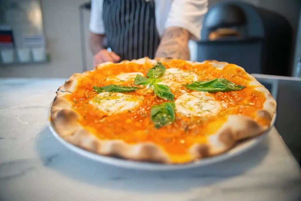 Close-up of freshly baked Margherita pizza with basil on a marble countertop.