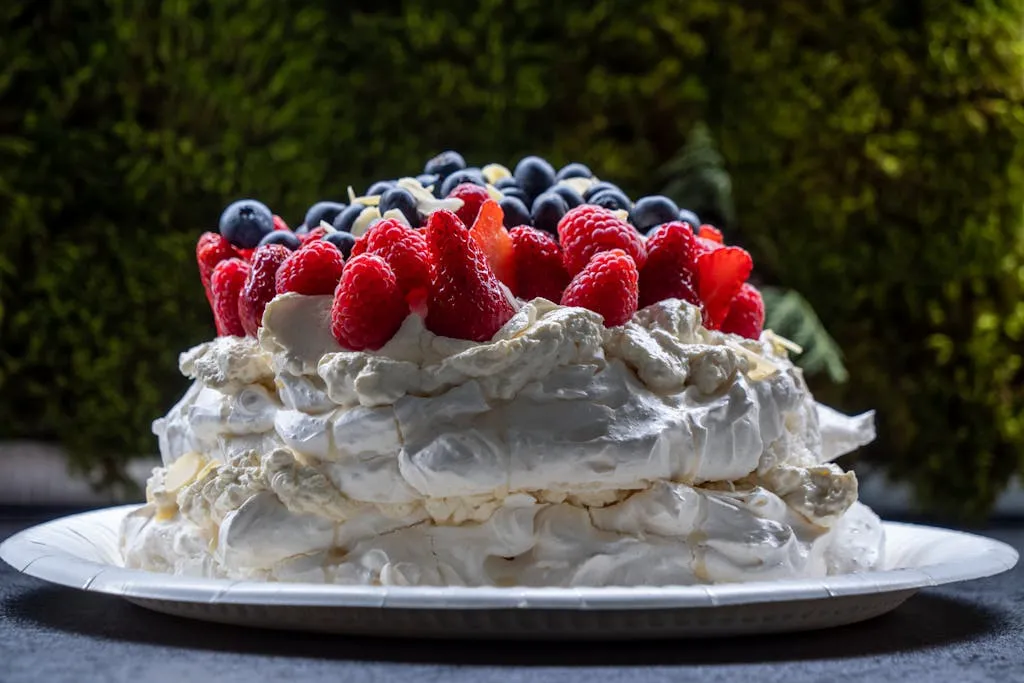Mouth-watering Pavlova cake topped with fresh strawberries, raspberries, and blueberries on a plate.
