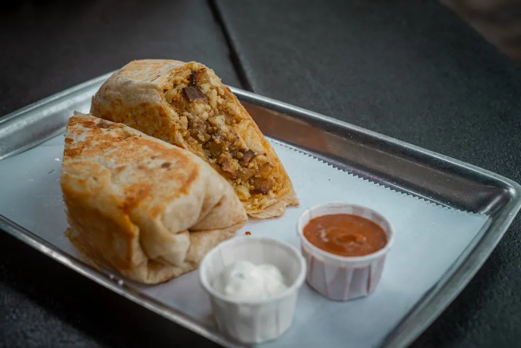 Tasty breakfast burrito served with salsa and sour cream on a metal tray.