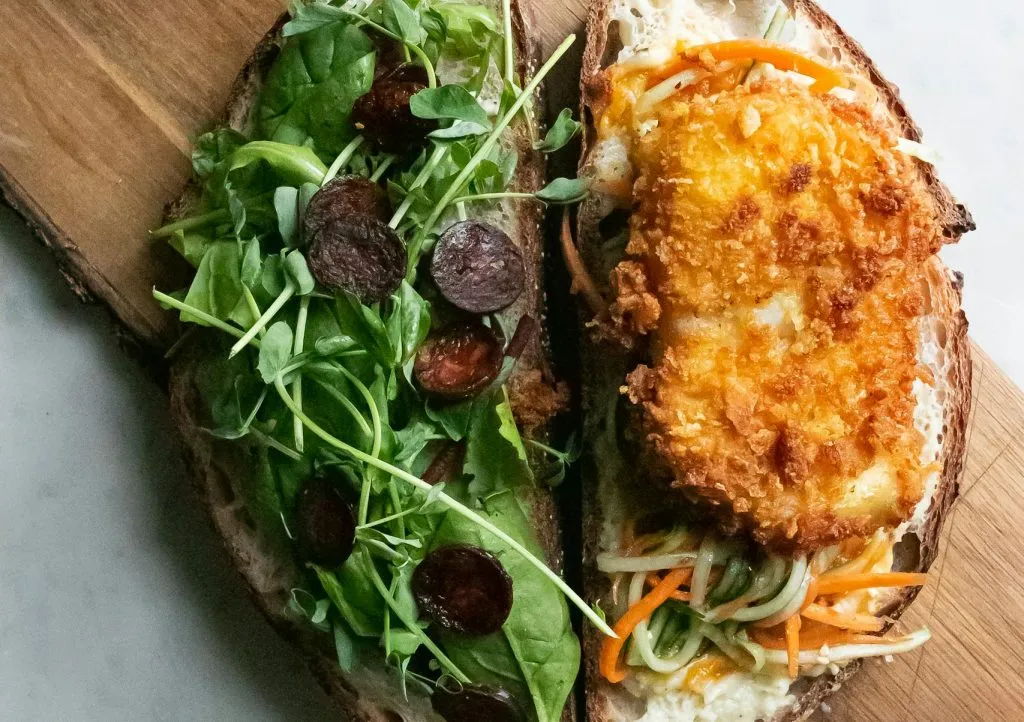 Top view of bruschettas with green rucola and fried chicken breast with vegetables served on wooden cutting board on table