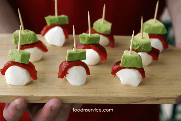 Mozzarella bites appetizer with fresh avocado and roasted red peppers on a wooden board.