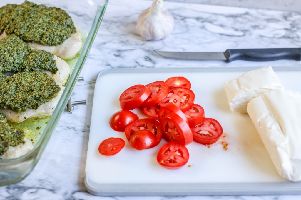 Basil pesto chicken ingredients overhead: chicken breasts, jar of basil pesto, fresh mozzarella, roma tomatoes, and seasonings.
