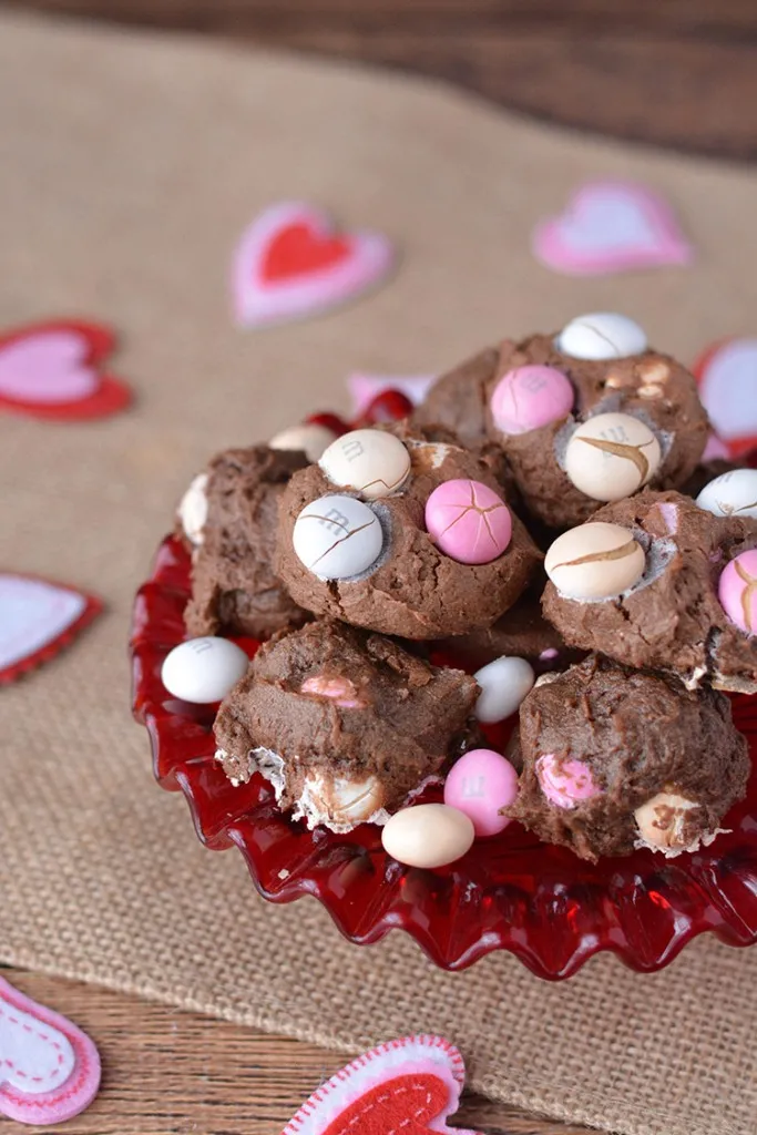 Multicolored M&Ms on chocolate cheesecake cookies on a red glass platter