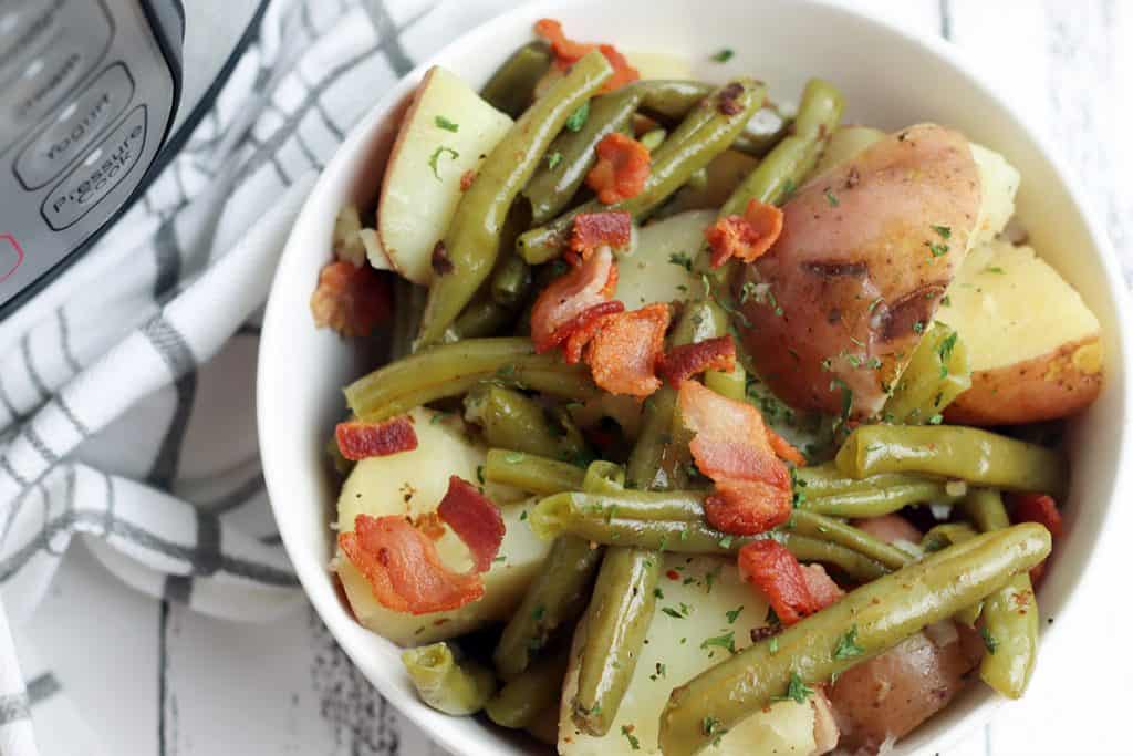 instant pot green beans and potatoes with bacon in a white bowl with a gray and white towel.
