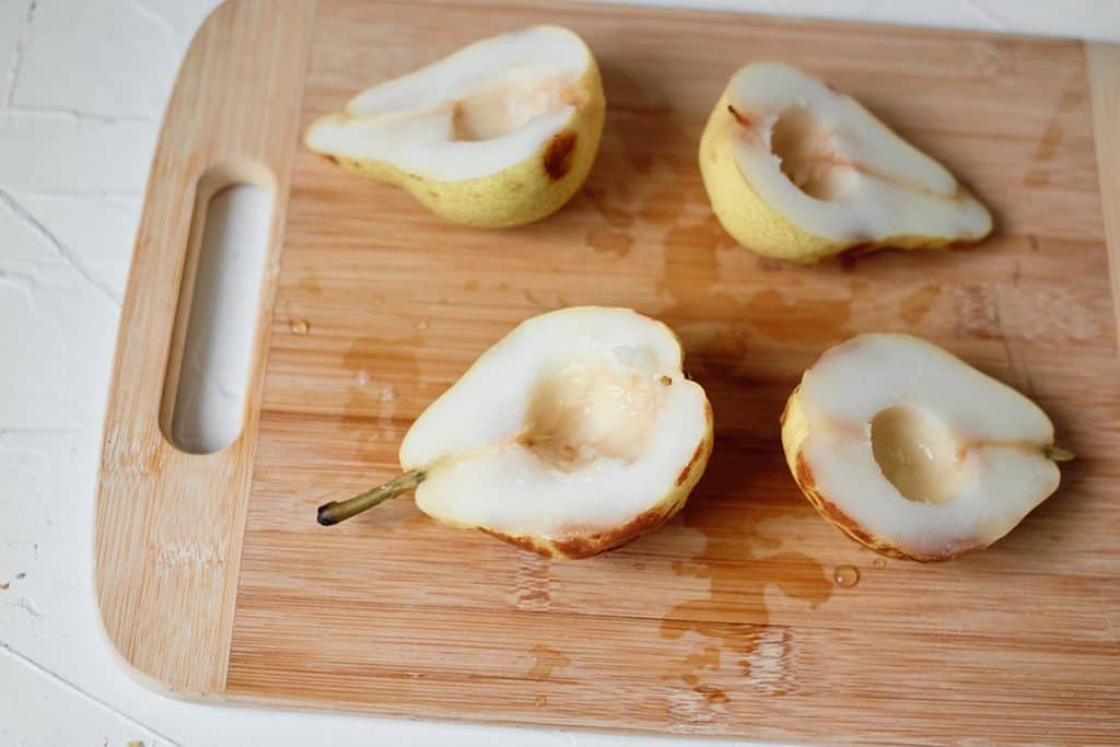 fresh cut pears on a wooden cutting board cut in half and holed
